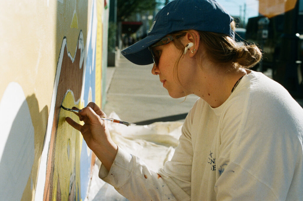 Artist Maxie Adler uses a paintbrush to work on her mural.