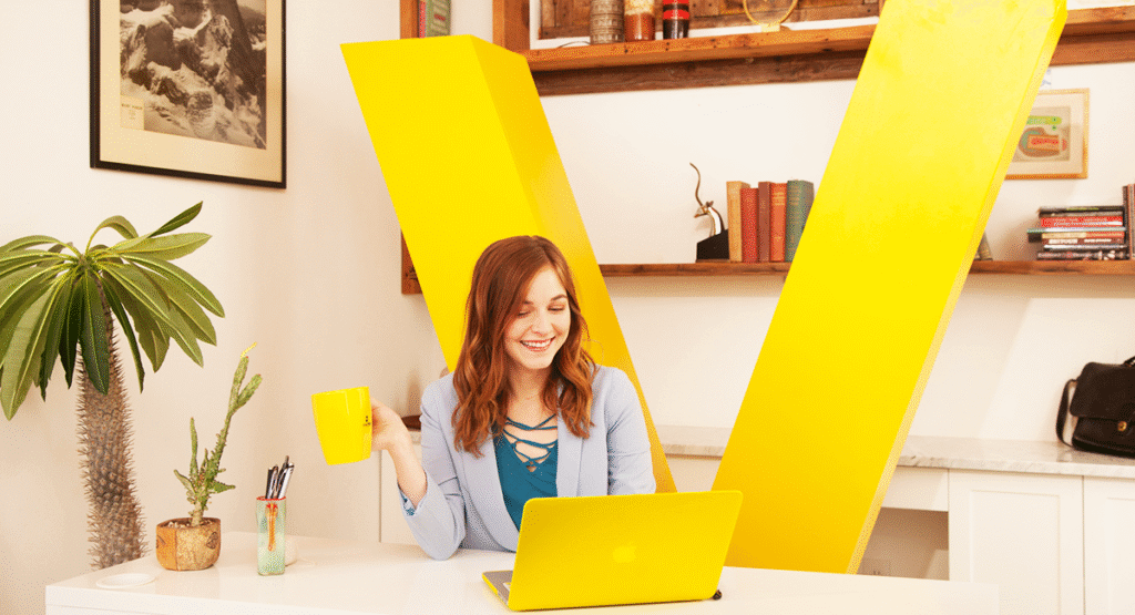 Woman smiling at computer screen holding coffee mug at desk