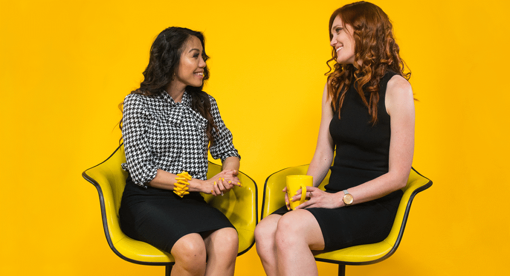 Two businesswomen sitting on yellow chairs and smiling, talking