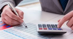 hand-holding-pen-with-other-hand-using-calculator-charting-data-at-desk
