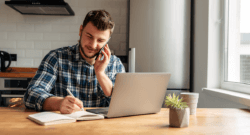 man-working-from-home-at-kitchen-tableon-the-phone-with-laptop