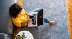 young girl in a yellow shirt woman working on a laptop at home using a smartphone in the living room on the carpet, distant work and education