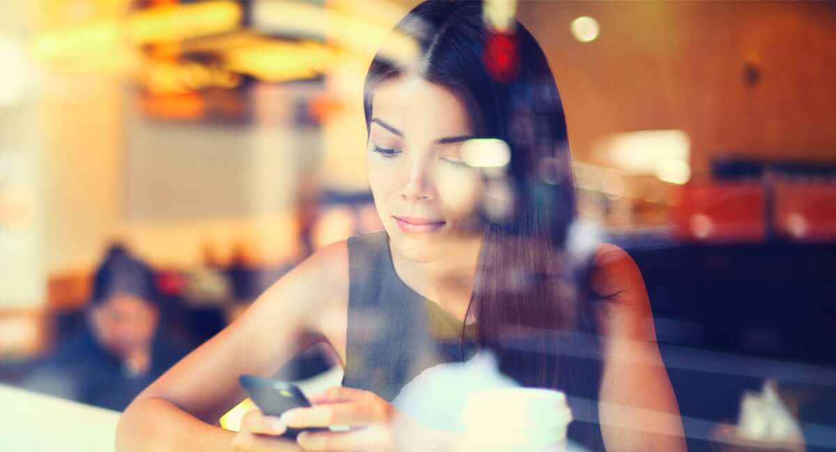 Through a window pane, a woman is seen checking her phone. 